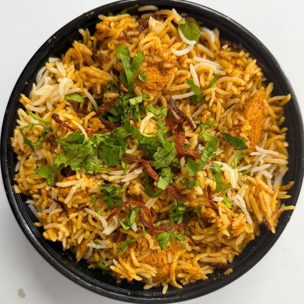 Chicken biryani with saffron-stained and white basmati rice, crispy fried onions and fresh coriander in a black bowl