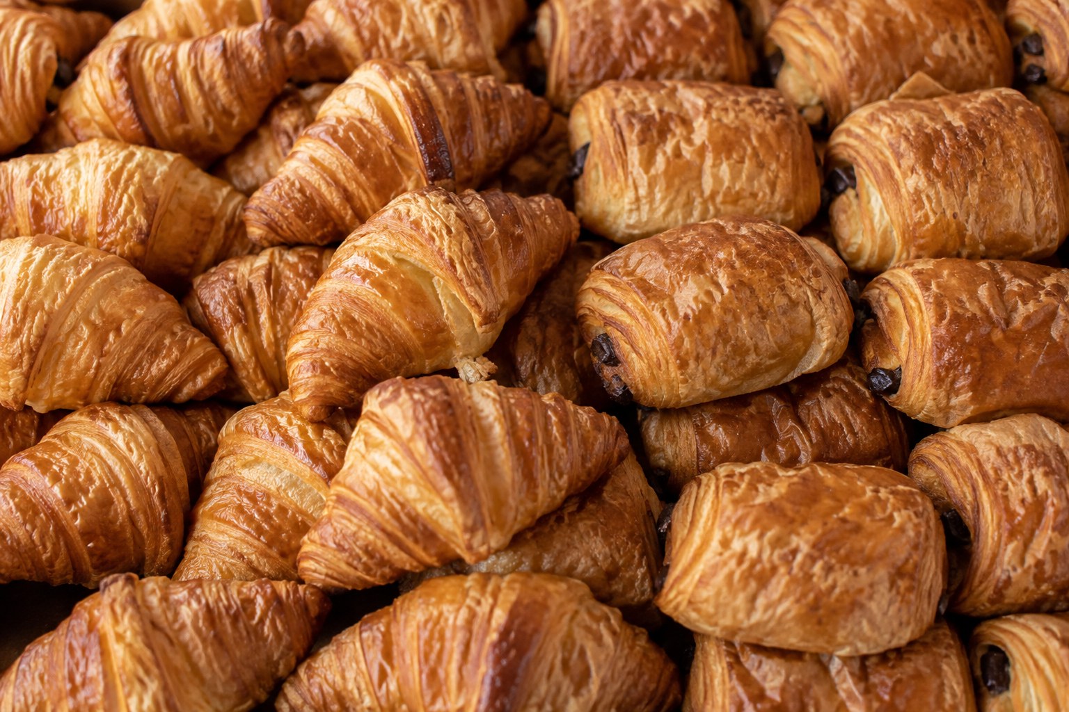 Butter croissants and mini pain au chocolat packed tightly together, freshly baked and golden